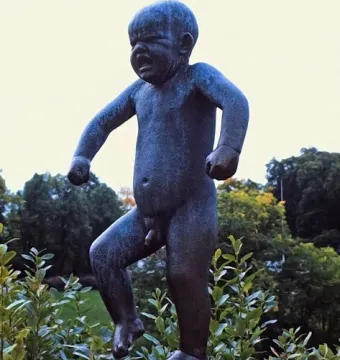 The Sinataggen bronze sculpture of a toddler stamping its foot on a pedestal, surrounded by trees.