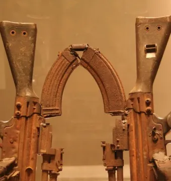 Throne of Weapons sculpture made from rusted firearm parts, with two rifle forms and arched magazines creating stylized faces.