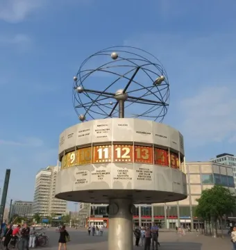The World Time Clock in Berlin, with city names and illuminated time panels beneath a spherical metal top in a public plaza.