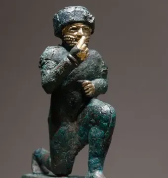 Worshipper of Larsa, a kneeling ancient figure with a raised hand and green patinated surface.