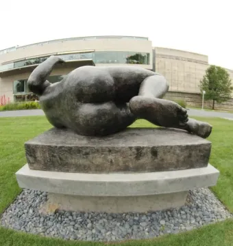 The River by Aristide Maillol, a dark recumbent nude sculpture on a pedestal in a sculpture garden.
