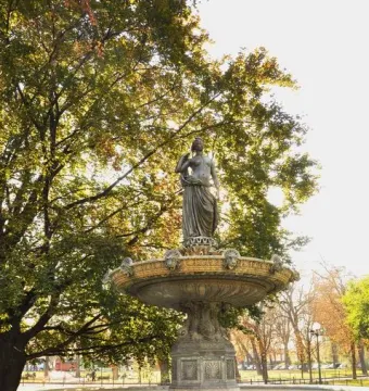 Diana Fountain in a grassy garden with autumn leaves and tall trees behind it.