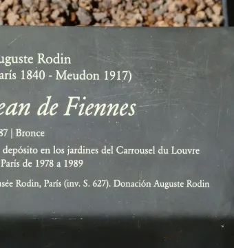Information plaque for Jean de Fiennes by Auguste Rodin with white text on a dark gray surface.