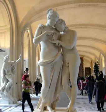 Standing Psyche and Love marble sculpture displayed on a pedestal in a museum gallery with visitors in the background.