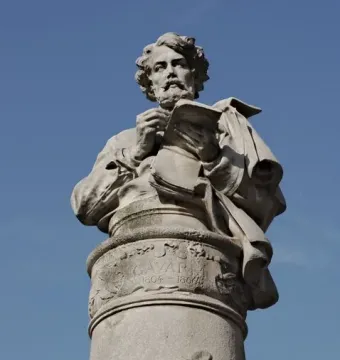 Gavarni Fountain stone sculpture with a carved figure holding an open book and pen against a blue sky