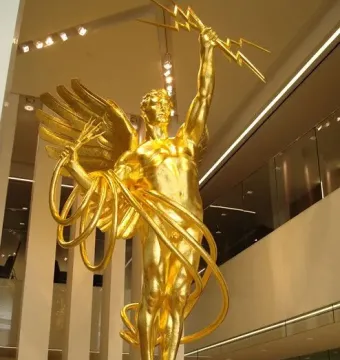 Golden Boy sculpture: a reflective golden winged man holding a lightning bolt and cable forms above a sphere