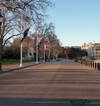 Horse Guards Memorial beside Horse Guards Road, with flagpoles, bollards, and a large historic building in the background.