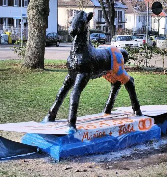 Holbeinpferd sculpture painted with an orange and blue pattern on its hindquarters, standing on a surfboard-like base.