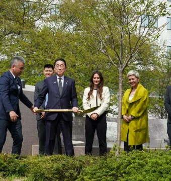 People in formal attire stand near the Japanese American Memorial with a gold shovel during a ceremonial gathering.