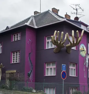Kristek House with a dark purple facade, magenta accents, golden hands, a melting figure on a clock, and a mural of a winding train track.