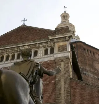 Back view of the Regisole bronze equestrian statue with a brick cathedral facade behind it.