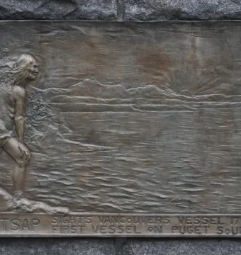 Bronze relief plaque on the Chief Seattle statue showing a figure looking toward the water, mountains, a rising sun, and a sailing ship.