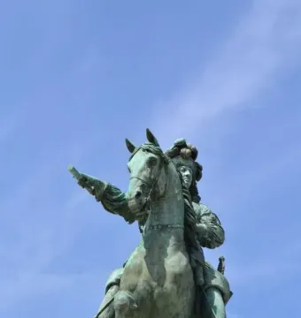 Equestrian Statue of Louis XIV, a green-patinated bronze rider on a rearing horse pointing forward against a blue sky.