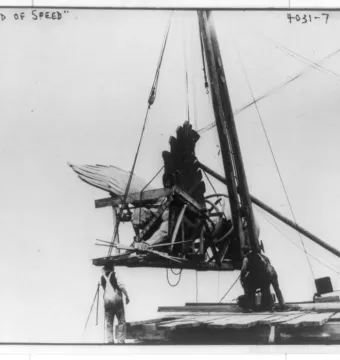Golden Boy statue being hoisted by cables and a wooden framework with workers below.