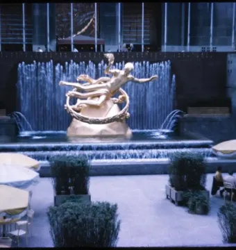 The Prometheus sculpture at Rockefeller Center, shown as a golden reclining figure holding up a ring above a tiered fountain.