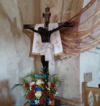 San Juan Patrón crucifix with a dark-skinned corpus, white loincloth, and red, white, and blue flowers below
