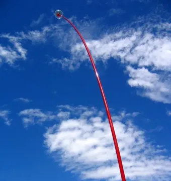 Wind Wand sculpture curving upward against a blue sky with scattered clouds.
