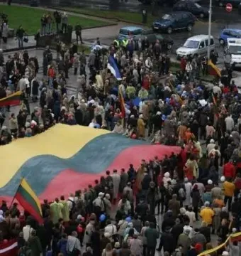 Large crowd holding a huge yellow green and red flag near the Bronze Soldier monument.