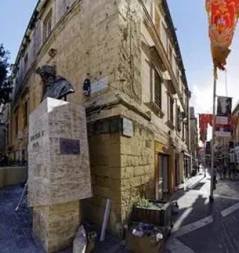 Great Siege Monument bronze bust on a tall stone pedestal near two red telephone booths in Valletta.
