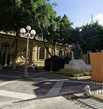 Great Siege Monument with three bronze figures in a sunny paved plaza surrounded by trees and historic buildings.