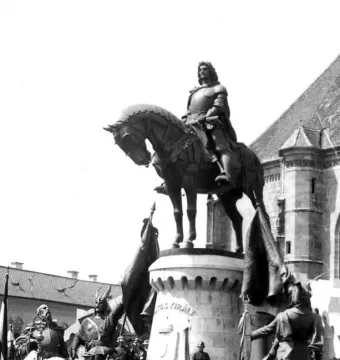 Matthias Corvinus Monument showing an armored rider on horseback atop a castellated stone pedestal, with figures and banners at the base.