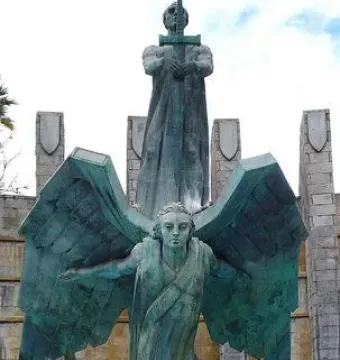 Monumento a Franco with a robed figure holding a cross-hilt sword above a winged figure on a stone base.