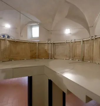 Reconstructed structure of the Pulpit of Prato Cathedral with a curved paneled railing inside a vaulted room.