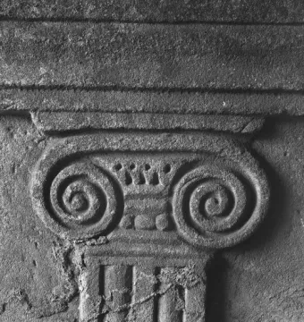 Close-up of an Ionic-style capital on the Sarcophagus of Louis the German, carved in weathered stone.