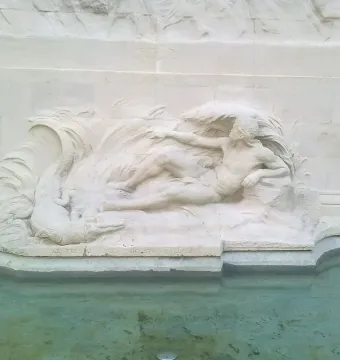 Relief sculpture from the Monument to the Belgian Pioneers in Congo showing a reclining figure, swirling water, and a crocodile-like creature above inscriptions reading \