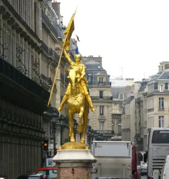Joan of Arc equestrian statue with a golden figure holding a standard on a stone pedestal in a city street.