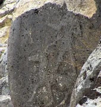 Karasu relief carved on a weathered dark stone slab among larger rocks.