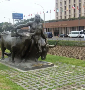 La yunta bronze sculpture of a man guiding two oxen on a lawn beside a patterned walkway.