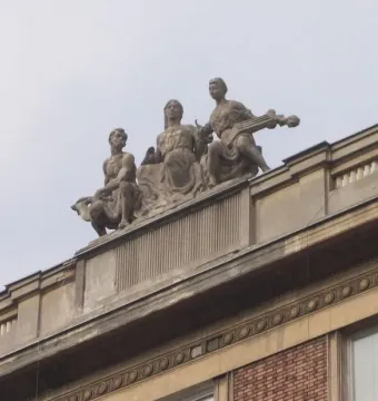 Three-figure Music sculpture on a rooftop, with a seated woman in the center, a figure holding an animal on the left, and a musician on the right.
