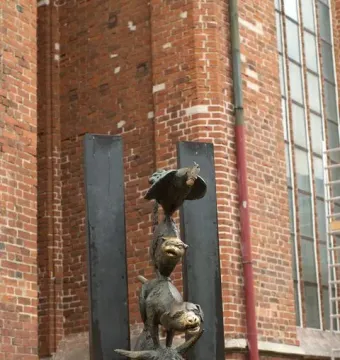 Bronze Bremer Stadtmusikanten sculpture with a donkey, dog, cat, and rooster stacked in a tower against a brick wall.
