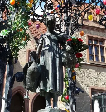 Gänseliesel Fountain with a bronze girl statue holding geese, decorated with Easter eggs and greenery.