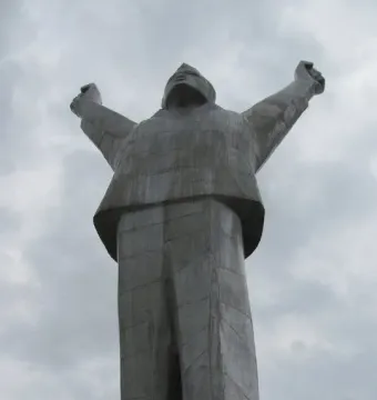 Monument to Stjepan Filipović seen from below, with the figure raising both arms against a cloudy sky.