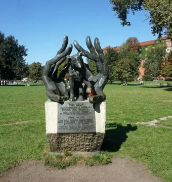 Bronze Monument to Dog Jock sculpture showing a dog nestled between two large hands on a stone pedestal in a park.