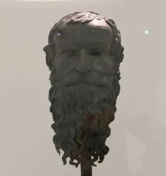 The Porticello Head bronze sculpture of an older man with a wavy beard and hollow eyes on a pedestal.