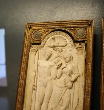 Queriniano Diptych ivory panel with a carved standing man and woman, a cherub, and a small animal beneath a shell-topped arch.