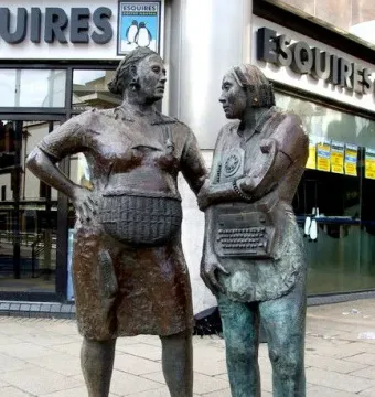 Monument to the Unknown Woman Worker, with two bronze women statues on a sidewalk beside a modern building.