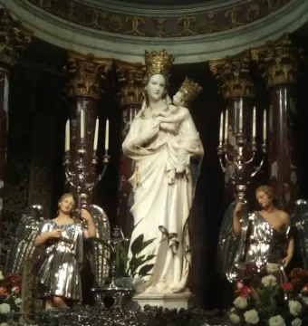 Crowned Madonna di Trapani statue holding the child, flanked by silver-clad angels with lit candelabras.