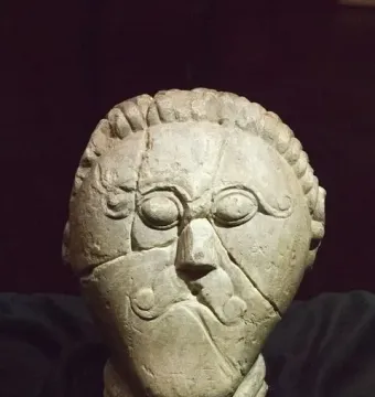Mšecké Žehrovice Head showing a carved stone face with oval eyes, a curled mustache, and a braided headdress.