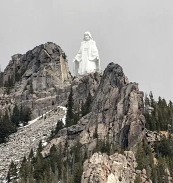 Our Lady of the Rockies statue standing on a rocky mountain peak with outstretched arms.