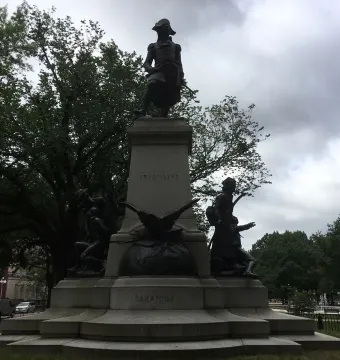 Tadeusz Kościuszko statue on a tall stone pedestal with smaller bronze figures and an eagle at the base.