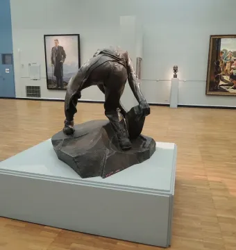 Cobblestone, a dark bronze headless figure crouching and holding a large stone.