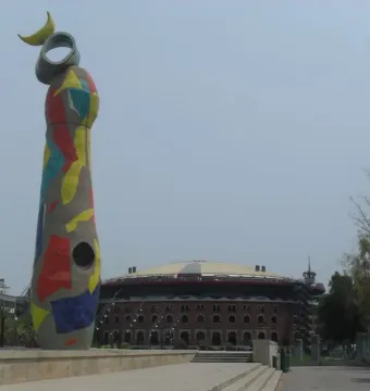 Dona i Ocell sculpture in Barcelona, covered in colorful mosaic tiles with a yellow crescent and ring at the top.