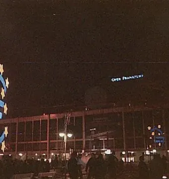 Illuminated Euro Sculpture with yellow stars in front of the Oper Frankfurt building at night.