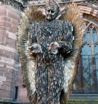 Knife Angel sculpture with outstretched hands and feathered wings outside a stone cathedral.