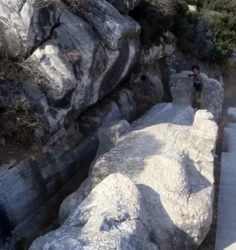 The unfinished Kouros of Apollonas лежing in a quarry, with a person standing beside its massive stone form.