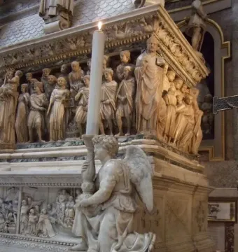 Michelangelo’s Angel sculpture shown kneeling and holding a tall candle on the Shrine of Saint Dominic.